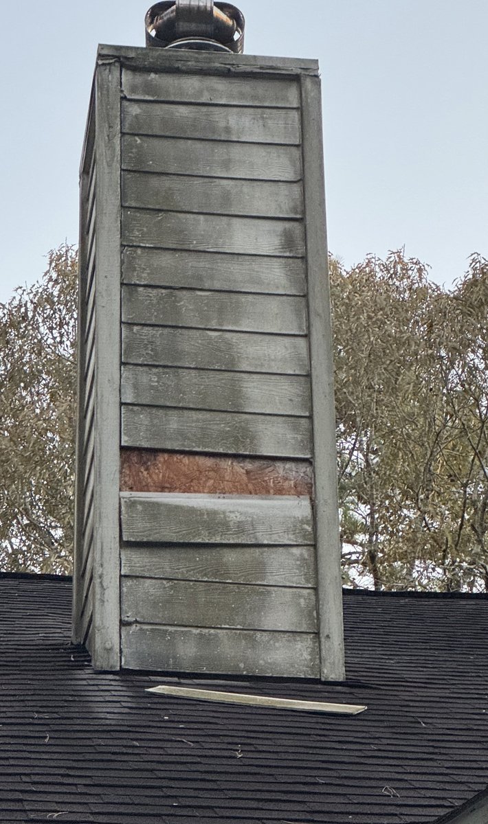 Chimney exterior before — weathered gray wood siding with rot patch