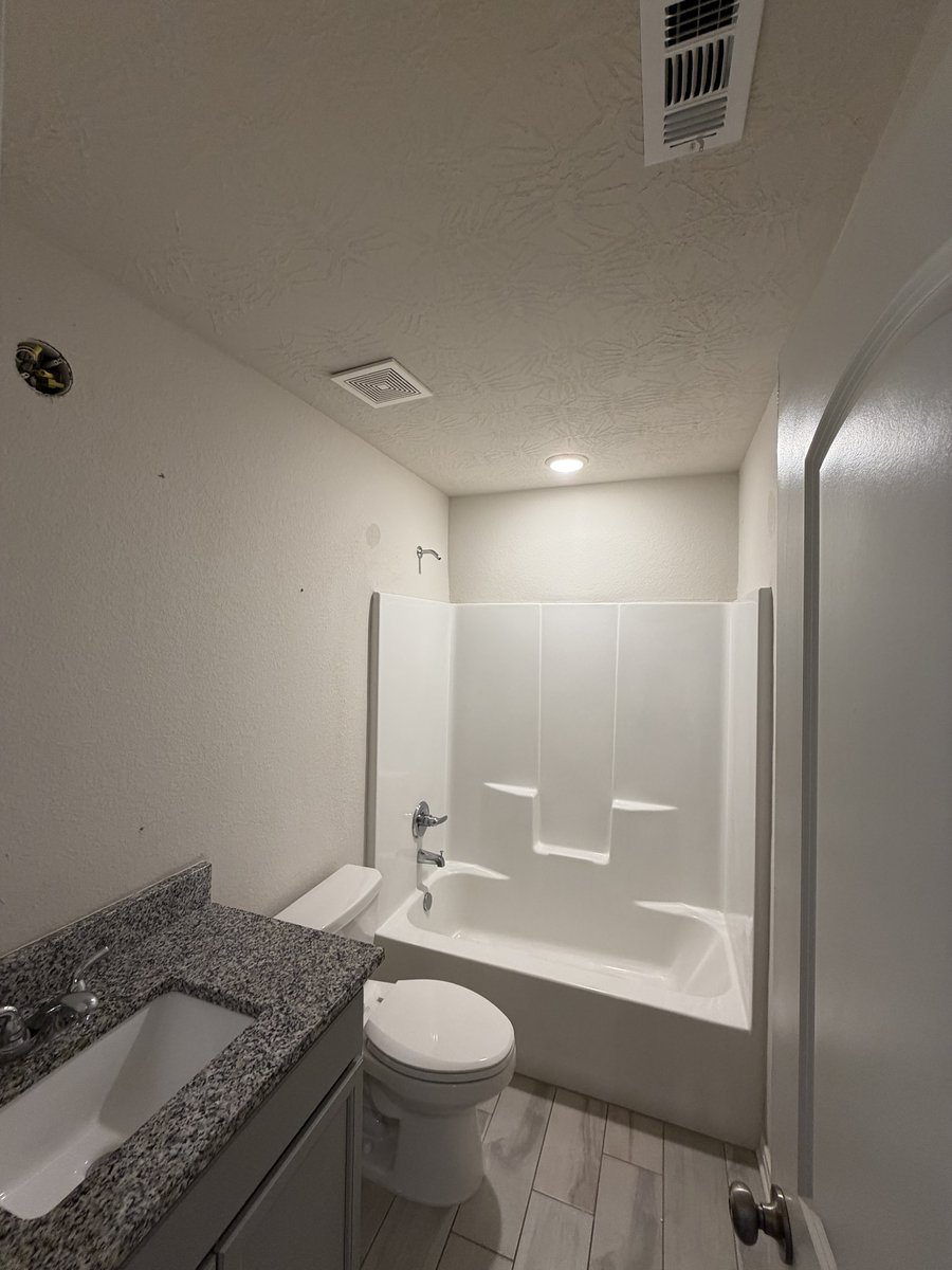 Powder room before — plain cream walls, white shower stall, builder-grade vanity