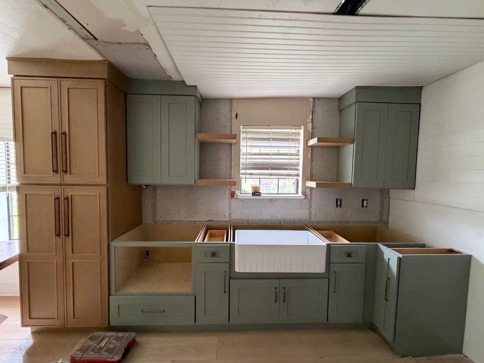 Sage green kitchen cabinets with farmhouse sink — install in progress